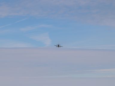 An airplane flying in the sky with clouds below at Plas Newydd in Llanfaelog near Rhosneigr