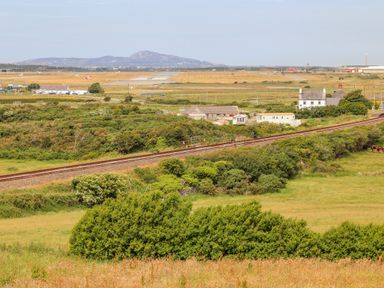 A rural landscape with railway tracks crossing fields and bushes with houses and an airstrip in the background at Plas Newydd Llanfaelog near Rhosneigr