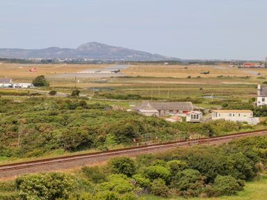 A rural landscape with railway tracks and farm buildings near an airport runway with distant hills in the background at Plas Newydd in Llanfaelog near Rhosneigr
