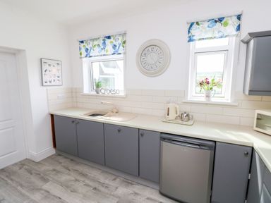 A kitchen with grey cabinets a sink a small fridge and windows with floral blinds at Garth in Pen-y-bryn near Cardigan
