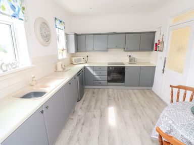 A kitchen with grey cabinets a sink an oven a microwave and a small dining table at Garth Pen-y-bryn near Cardigan