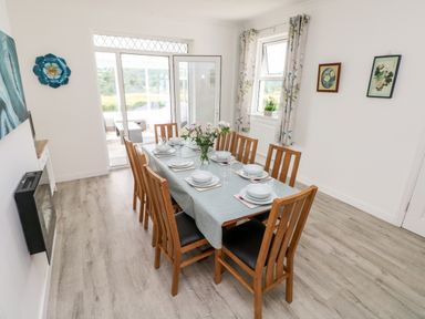 A dining room with a wooden table and chairs set for six with a flower vase and glass doors at Garth in Pen-y-bryn near Cardigan