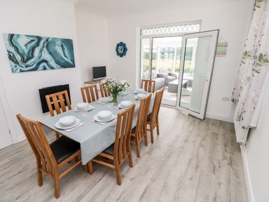 A dining room with a wooden table and chairs set for a meal next to a door leading to a sunroom at Garth in Pen-y-bryn near Cardigan