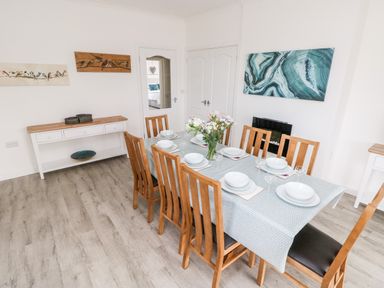 A dining room with a table set for six with flowers and artwork on white walls at Garth in Pen-y-bryn near Cardigan