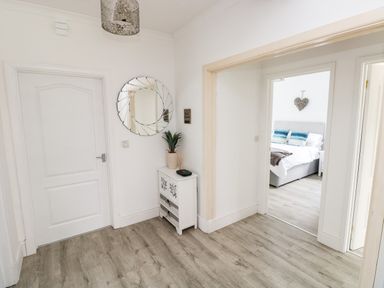 A hallway with a white door a decorative mirror above a small cabinet and a bedroom visible through an open doorway at Garth in Pen-y-bryn near Cardigan