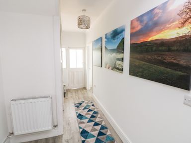 A hallway with a radiator on the left wall geometric patterned rug on the floor three landscape photos on the right wall a white door at the end of the hall at Garth in Pen-y-bryn near Cardigan