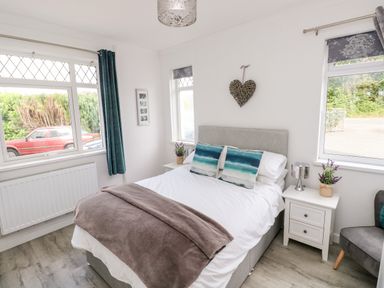 A bedroom with a double bed two decorative pillows bedside tables and windows at Garth in Pen-y-bryn near Cardigan