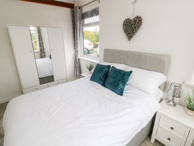 A bedroom with a double bed with white bedding and blue cushions beside a window with grey curtains and a white wardrobe at Garth in Pen-y-bryn near Cardigan