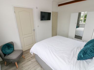 A bedroom with a bed a wall-mounted TV a chair with a cushion and a wardrobe with mirrored doors at Garth in Pen-y-bryn near Cardigan