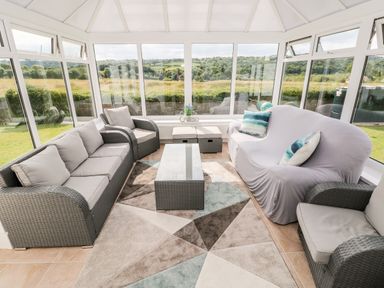 A sunroom with wicker sofas and a glass table overlooking fields at Garth in Pen-y-bryn near Cardigan