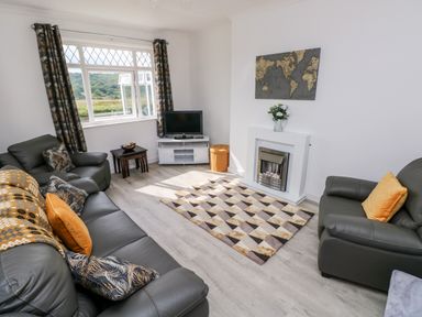 A living room with grey leather sofas a patterned rug a TV on a stand and a fireplace at Garth in Pen-y-bryn near Cardigan