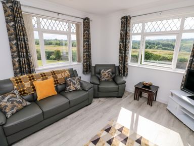 A living room with green sofas, patterned cushions, dark curtains, small tables, and a television at Garth in Pen-y-bryn near Cardigan