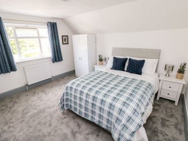 A bedroom with a double bed with checkered bedding two nightstands with lamps and plants a white wardrobe and a window with blue curtains at Garth in Pen-y-bryn near Cardigan
