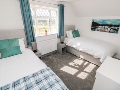 A bedroom with two single beds bedside tables lamps blue curtains and a window at Garth in Pen-y-bryn near Cardigan