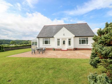A white house with a dark roof and a patio with chairs and a table on a lawn at Garth in Pen-y-bryn near Cardigan