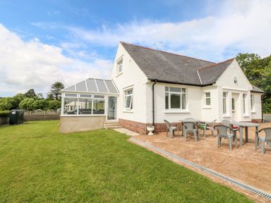 A single-story house with a glass conservatory lawn and patio with plastic chairs and tables at Garth in Pen-y-bryn near Cardigan