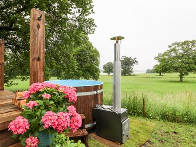 An outdoor hot tub next to wooden steps and pink flowers overlooking a grassy field at The Lazy Mare by The Water Admaston near Abbots Bromley