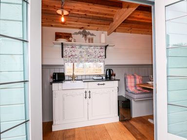 A small kitchen area with a white cabinet sink toaster kettle and a built in dining bench at The Lazy Mare by The Water in Admaston near Abbots Bromley
