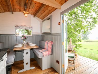 A dining area with a table set for four and bench seating with cushions next to an open door to a wooden deck at The Lazy Mare by The Water Admaston near Abbots Bromley