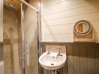 A bathroom with a shower cubicle a sink with two taps and a round mirror on the wall at The Lazy Mare by The Water Admaston near Abbots Bromley