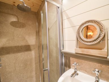 A bathroom with a shower, sink with faucets, and a round mirror on a shelf at The Lazy Mare by The Water Admaston near Abbots Bromley