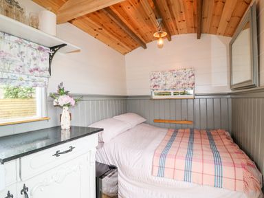A bedroom with a bed a small dresser with a flower vase and two windows with floral blinds at The Lazy Mare by The Water Admaston near Abbots Bromley