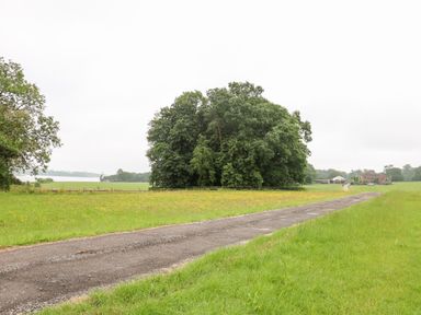A rural landscape with a gravel road running through green fields and trees at The Lazy Mare by The Water Admaston near Abbots Bromley