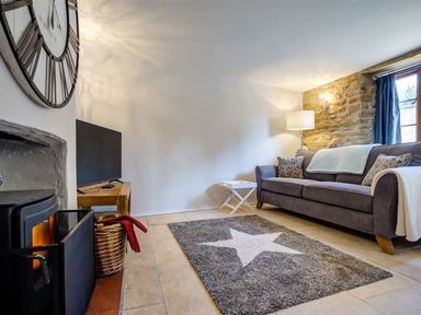 A living room with a sofa a rug with a star a fireplace and a wall clock at Hollytree Cottage in Hook Norton