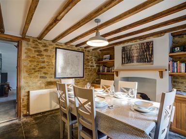 A dining room with a table set for six and wooden beams on the ceiling at Hollytree Cottage in Hook Norton