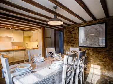 A dining area with a table set for six and a kitchen in the background at Hollytree Cottage in Hook Norton