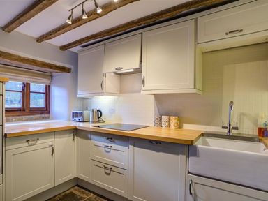 A kitchen with wooden countertops white cabinets and a farmhouse sink at Hollytree Cottage in Hook Norton