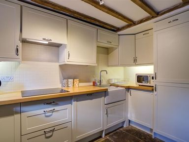 A kitchen with white cabinets wooden countertops a sink microwave and ceramic tiles at Hollytree Cottage in Hook Norton