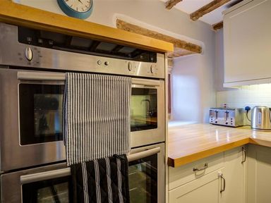 A kitchen with double oven a wooden countertop toaster kettle and striped towels at Hollytree Cottage in Hook Norton