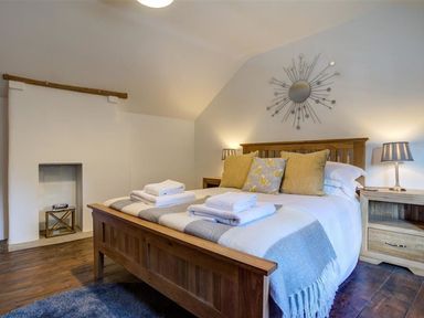 A bedroom with a wooden bed with pillows and towels bedside tables with lamps a circular decorative mirror on the wall at Hollytree Cottage in Hook Norton