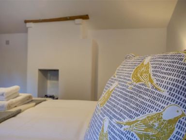 A close up of a pillow with bird patterns on a bed with folded towels in a bedroom at Hollytree Cottage in Hook Norton
