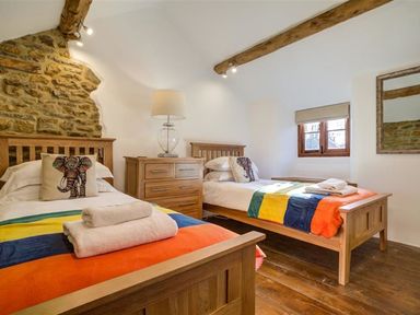 A bedroom with two wooden single beds with colorful blankets a wooden chest of drawers and a window at Hollytree Cottage in Hook Norton