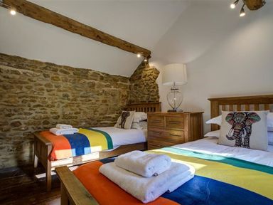 A bedroom with two single beds a chest of drawers and a lamp at Hollytree Cottage in Hook Norton