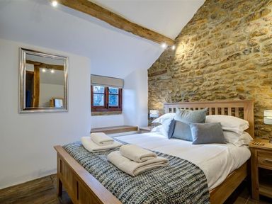 A bedroom with a wooden bed frame stone wall bedside tables and a window at Hollytree Cottage in Hook Norton