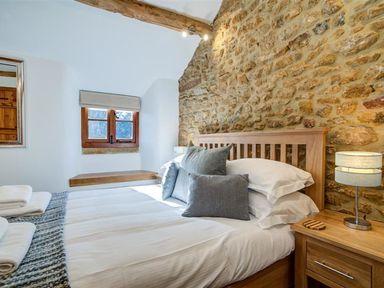 A bedroom with a wooden bed frame and stone wall at Hollytree Cottage in Hook Norton
