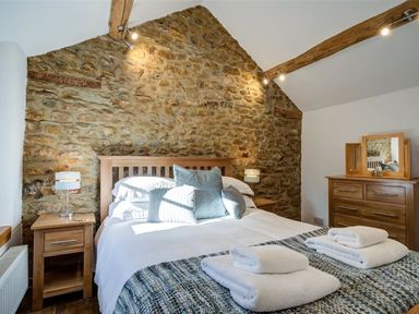 A bedroom with a wooden bed and nightstands against a stone wall at Hollytree Cottage in Hook Norton