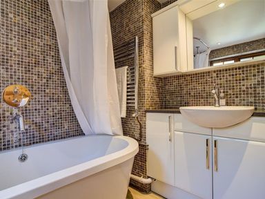 A bathroom with a bathtub shower curtain sink mirror and white cabinets at Hollytree Cottage in Hook Norton