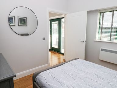 A bedroom with a bed a window with blinds a door leading to another room and a round wall mirror at Ramsey Cottage in Milford Haven