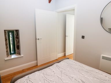A bedroom with a bed partially visible a small window with stone trim two white doors and a round mirror on the wall at Ramsey Cottage in Milford Haven