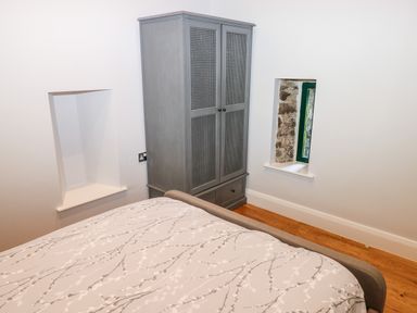 A bedroom with a bed, a gray wardrobe, and two small window openings at Ramsey Cottage in Milford Haven