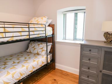 A bedroom with bunk beds next to a window and a gray dresser with a lamp at Ramsey Cottage in Milford Haven