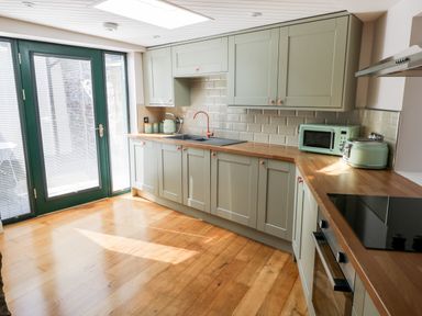 A kitchen with green cabinets wooden countertops and green appliances at Ramsey Cottage in Milford Haven