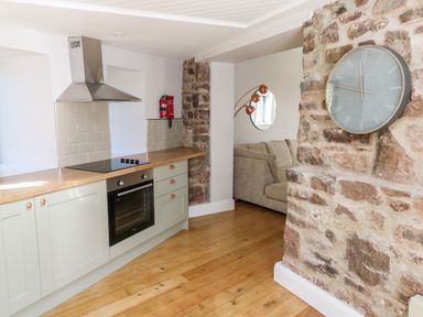 A kitchen with wooden floor wooden countertop gray cabinets stovetop oven and stone wall with clock at Ramsey Cottage in Milford Haven