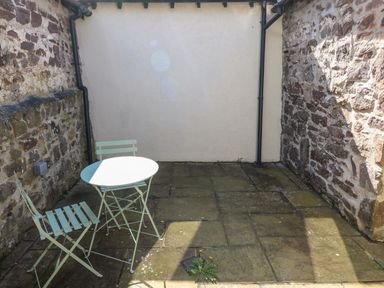 A small outdoor patio area with stone walls two metal chairs and a round metal table at Ramsey Cottage in Milford Haven