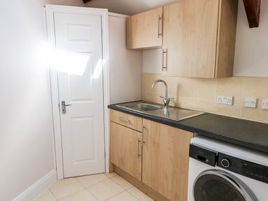 A kitchen with wooden cabinets a sink washing machine and a closed white door at Ramsey Cottage in Milford Haven