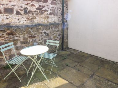 An outdoor patio with stone walls and a white round table with two metal chairs at Ramsey Cottage in Milford Haven